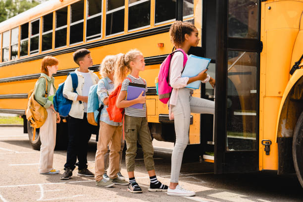 Schoolchildren kids pupils group of mixed-race classmates boarding school bus before going to lessons, coming back to school, standing in line. New educational year semester.